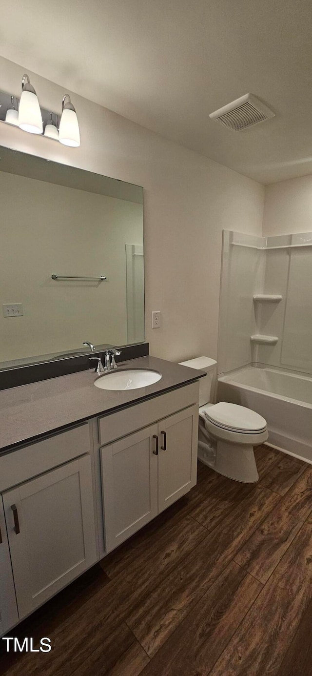 full bathroom with hardwood / wood-style flooring, vanity, shower / washtub combination, and toilet