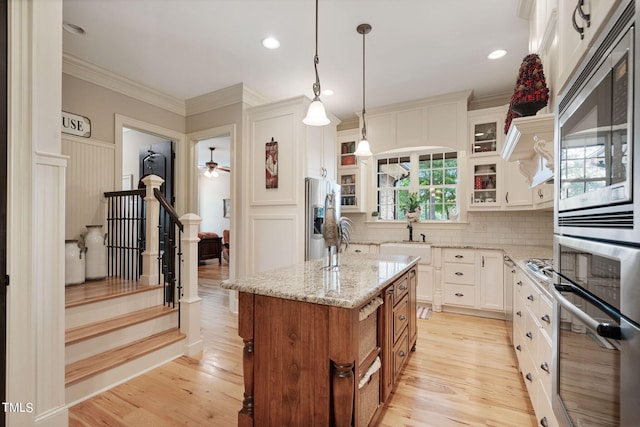 kitchen with appliances with stainless steel finishes, white cabinets, hanging light fixtures, a center island, and light stone countertops