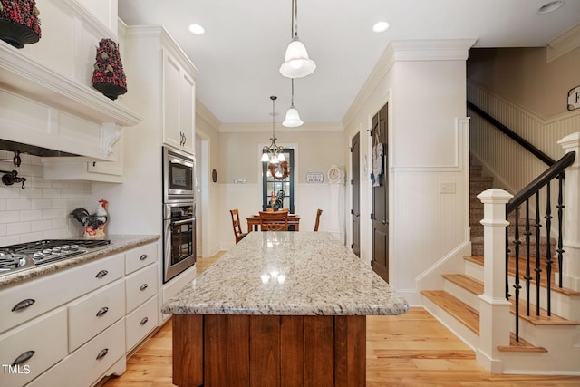 kitchen with crown molding, a kitchen island, stainless steel appliances, light hardwood / wood-style floors, and white cabinets