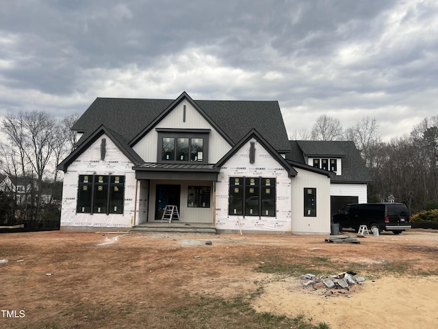 back of property featuring metal roof, roof with shingles, a standing seam roof, and a garage