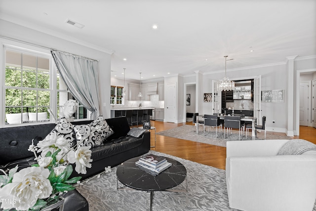 living room with crown molding, light wood-type flooring, and a chandelier