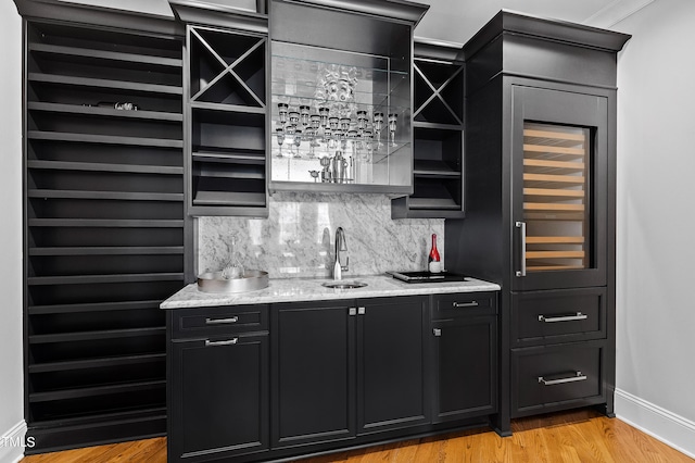 bar with light hardwood / wood-style flooring, light stone countertops, tasteful backsplash, and sink