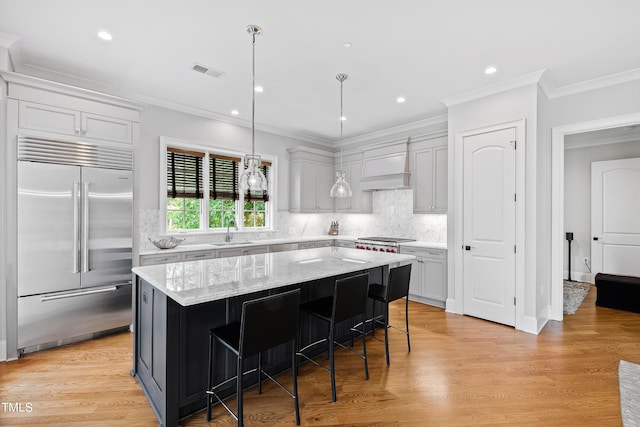 kitchen with built in refrigerator, custom exhaust hood, a sink, ornamental molding, and visible vents