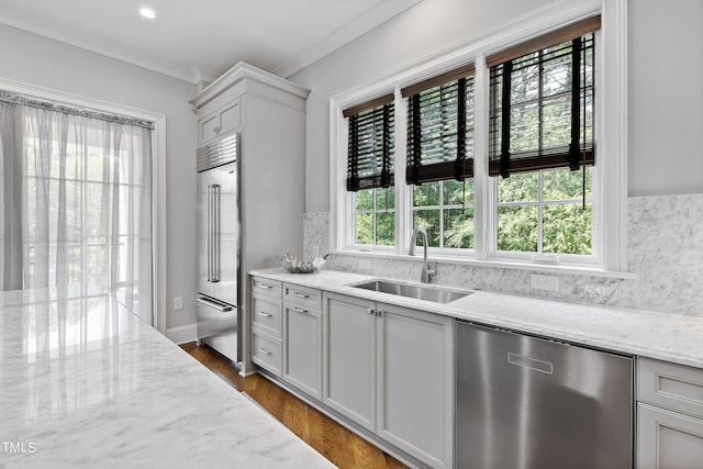 kitchen featuring a sink, decorative backsplash, appliances with stainless steel finishes, light stone countertops, and ornamental molding