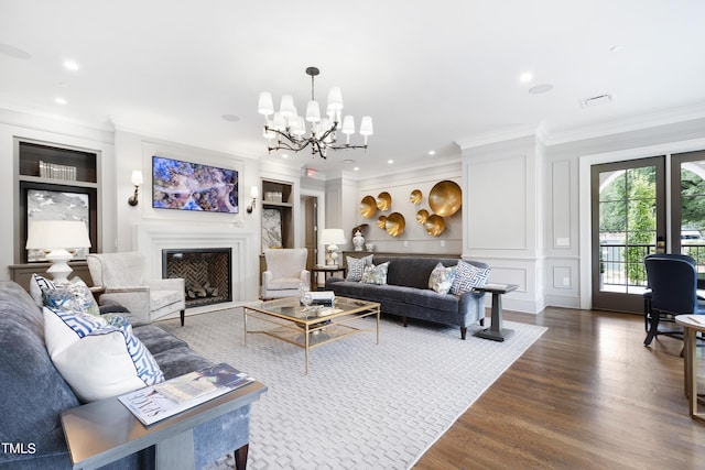 living room featuring built in features, a notable chandelier, wood finished floors, a fireplace, and ornamental molding