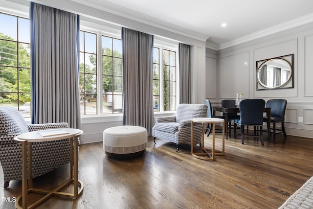 living area with a decorative wall, ornamental molding, and wood finished floors