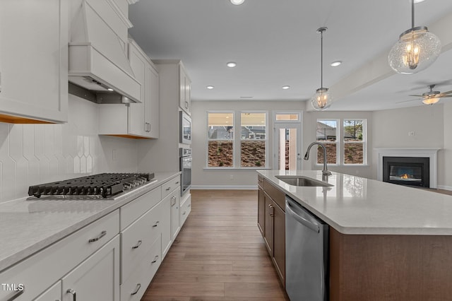 kitchen featuring a kitchen island with sink, premium range hood, sink, white cabinetry, and stainless steel appliances