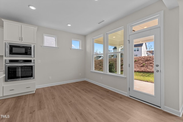 kitchen with black microwave, stainless steel oven, white cabinets, and light hardwood / wood-style flooring