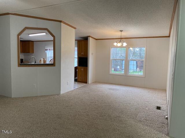 unfurnished room with a textured ceiling, crown molding, light carpet, and a notable chandelier