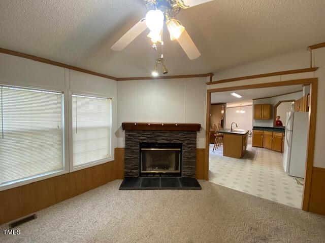 living room with a fireplace, a textured ceiling, ceiling fan, ornamental molding, and light colored carpet