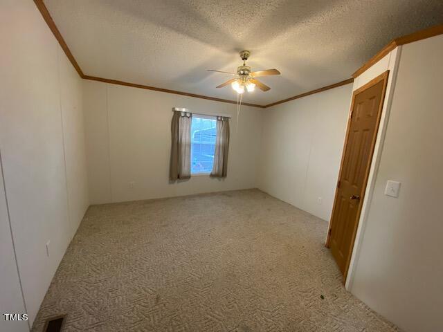 carpeted spare room with a textured ceiling, crown molding, and ceiling fan