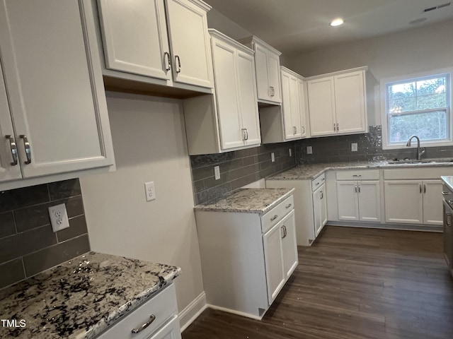 kitchen featuring sink, backsplash, dark hardwood / wood-style floors, light stone countertops, and white cabinets