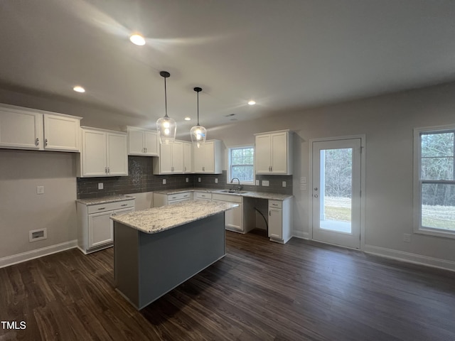 kitchen featuring a kitchen island, decorative light fixtures, sink, white cabinets, and light stone counters