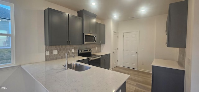 kitchen with light stone counters, light wood-style flooring, decorative backsplash, appliances with stainless steel finishes, and a sink