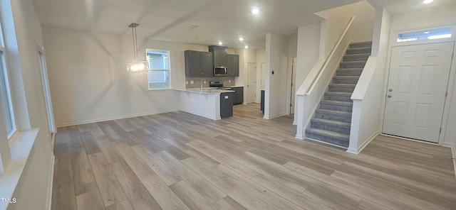 kitchen featuring stainless steel microwave, open floor plan, a peninsula, light countertops, and light wood-type flooring