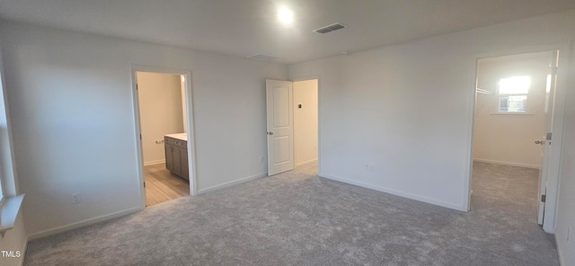 unfurnished bedroom with light carpet, connected bathroom, visible vents, and baseboards