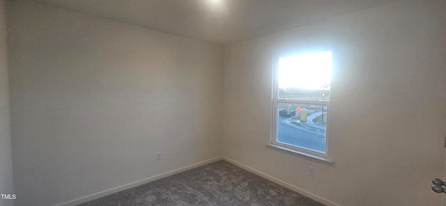 spare room with baseboards and dark colored carpet