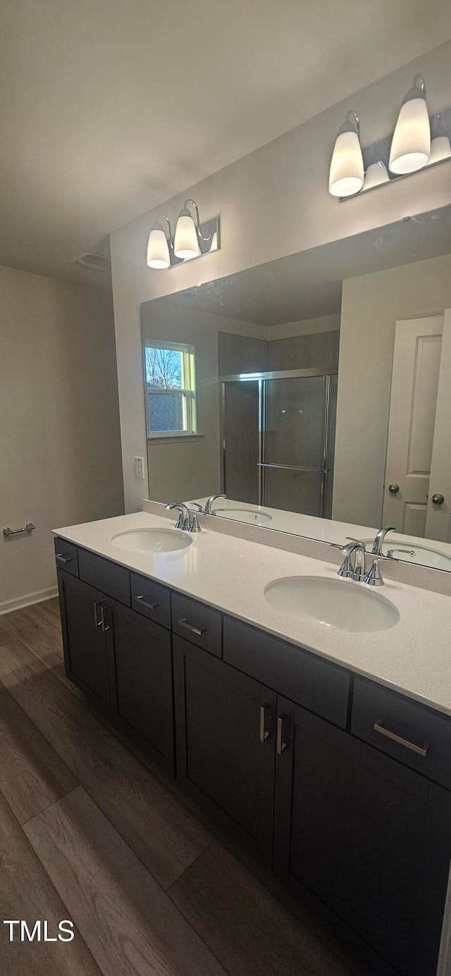 bathroom featuring double vanity, a stall shower, a sink, and wood finished floors