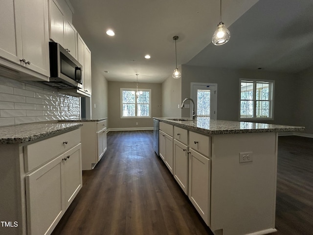 kitchen with dark wood-type flooring, a sink, white cabinets, decorative backsplash, and stainless steel microwave