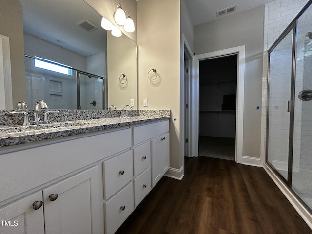 full bathroom with double vanity, a shower stall, visible vents, and wood finished floors