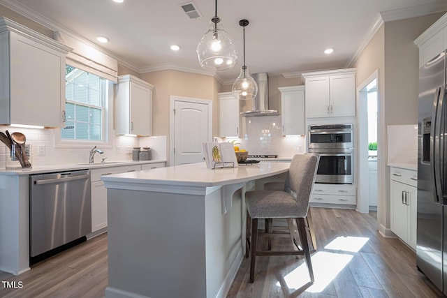 kitchen featuring white cabinets, a center island, stainless steel appliances, light countertops, and wall chimney range hood