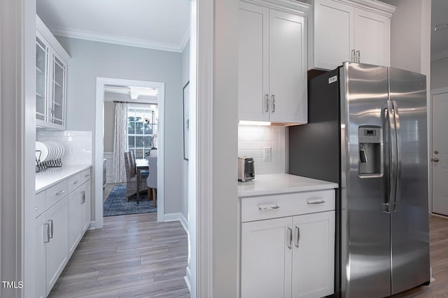 kitchen featuring white cabinets, light countertops, ornamental molding, stainless steel fridge, and glass insert cabinets