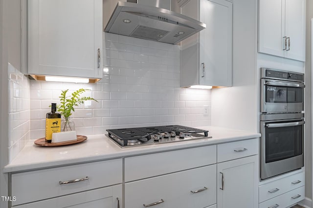 kitchen featuring white cabinets, wall chimney exhaust hood, light countertops, stainless steel appliances, and backsplash