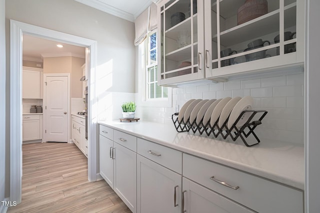 kitchen with light countertops, white cabinetry, glass insert cabinets, and crown molding