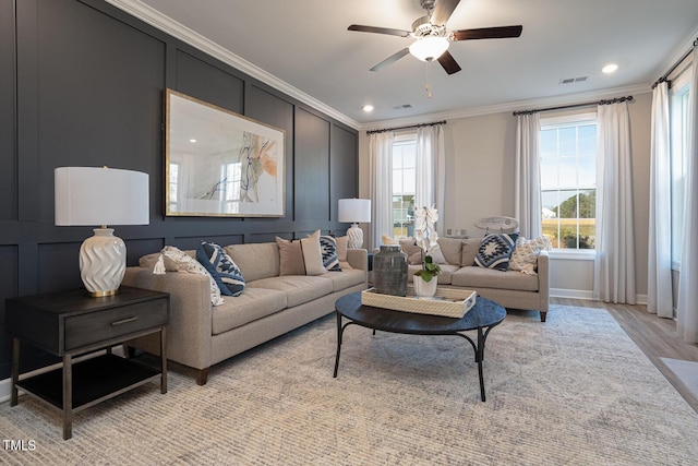 living area featuring visible vents, a ceiling fan, ornamental molding, light wood-type flooring, and a decorative wall