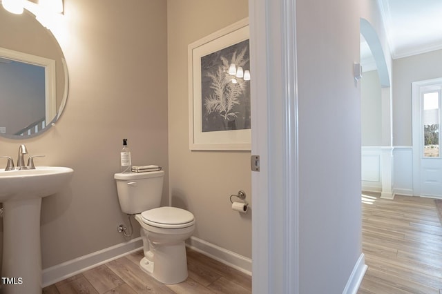 bathroom with baseboards, toilet, wood finished floors, crown molding, and a sink