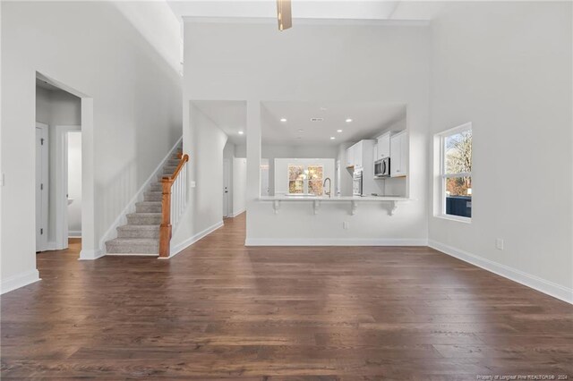 unfurnished living room with sink, dark wood-type flooring, and a high ceiling