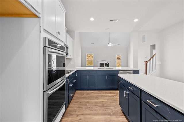 kitchen featuring ceiling fan, sink, double oven, white cabinets, and light wood-type flooring