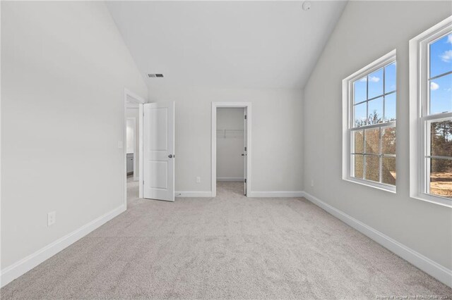 unfurnished bedroom with a closet, a walk in closet, light carpet, and vaulted ceiling