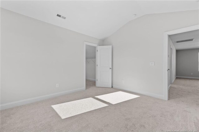 unfurnished bedroom featuring a walk in closet, light carpet, and vaulted ceiling