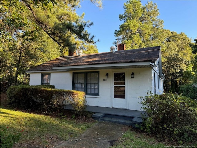 view of front of house with a chimney, covered porch, and concrete block siding