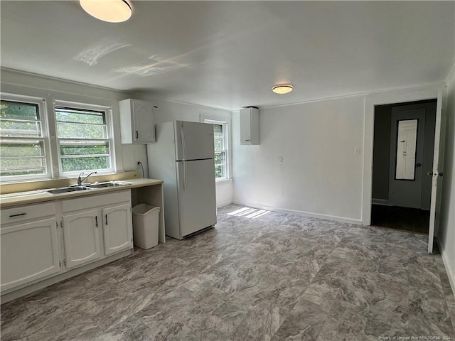kitchen with light countertops, a sink, freestanding refrigerator, white cabinetry, and baseboards