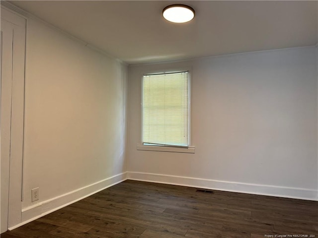 spare room featuring dark wood finished floors, baseboards, visible vents, and crown molding