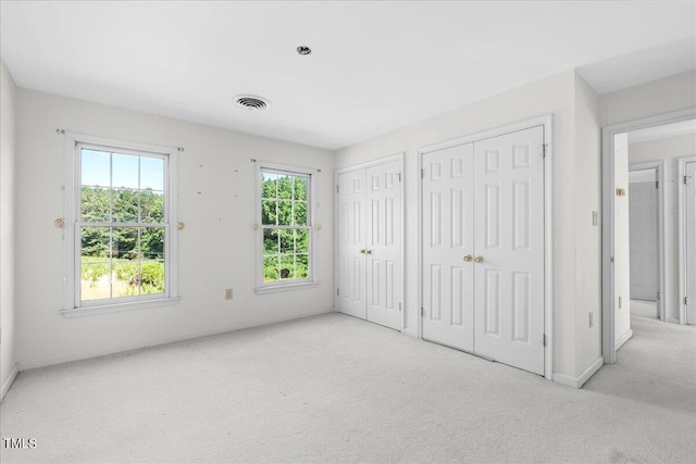 unfurnished bedroom with light colored carpet and two closets