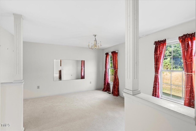 carpeted spare room featuring decorative columns, plenty of natural light, and a notable chandelier