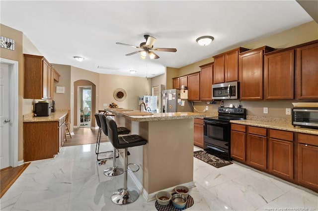 kitchen featuring ceiling fan, a kitchen island, a kitchen bar, and appliances with stainless steel finishes