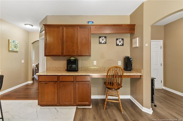 kitchen with light stone counters, built in desk, and wood-type flooring