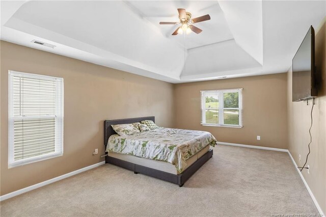 carpeted bedroom with a raised ceiling and ceiling fan