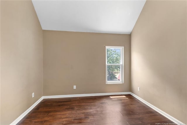 empty room featuring baseboards, vaulted ceiling, and dark wood-type flooring