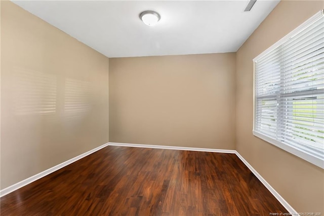 empty room featuring dark wood-style flooring, visible vents, and baseboards