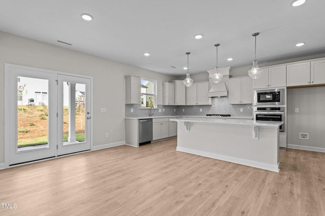 kitchen featuring a center island, pendant lighting, a breakfast bar area, white cabinets, and light wood-type flooring