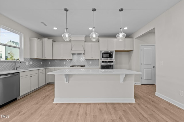 kitchen with white cabinets, a kitchen island, light wood-type flooring, and stainless steel appliances