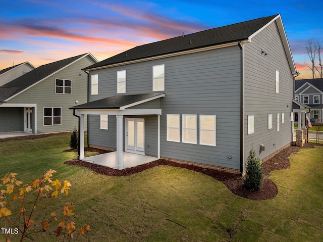 back house at dusk with a lawn and a patio