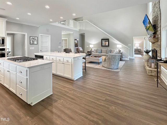 kitchen featuring appliances with stainless steel finishes, a stone fireplace, a center island, white cabinets, and dark wood-type flooring