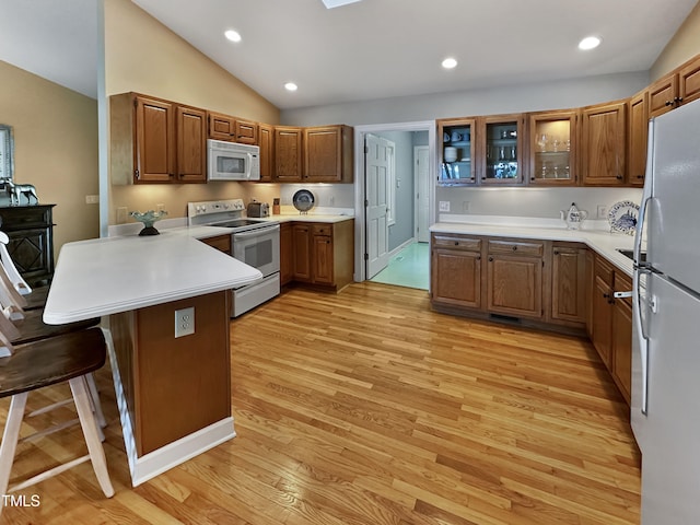 kitchen featuring kitchen peninsula, a kitchen breakfast bar, white appliances, light wood-type flooring, and vaulted ceiling