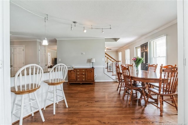 dining space featuring rail lighting, a textured ceiling, dark hardwood / wood-style flooring, and ornamental molding